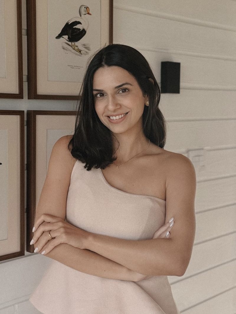 Rayane Mirella, psicóloga, sorrindo de braços cruzados em seu consultório